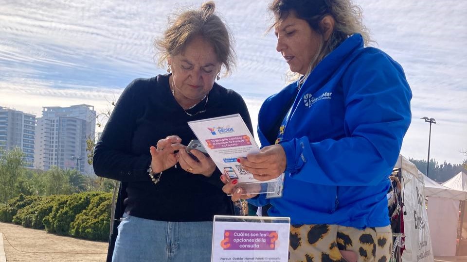 Mujer en chaqueta municipal ayuda a otra mujer ingresar a una encuesta digital